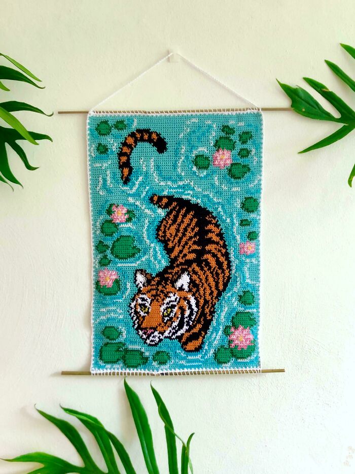 Crochet wall hanging featuring a detailed tiger design surrounded by lily pads and flowers, showcasing crochet masterpieces.