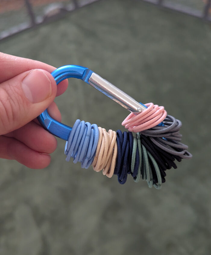 Close-up of hand holding a blue carabiner with colorful hair ties, illustrating dads doing their best parenting moments.
