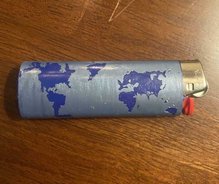 A lighter with blue continents painted on it, resembling a world map, on a wooden surface; mildly interesting design.