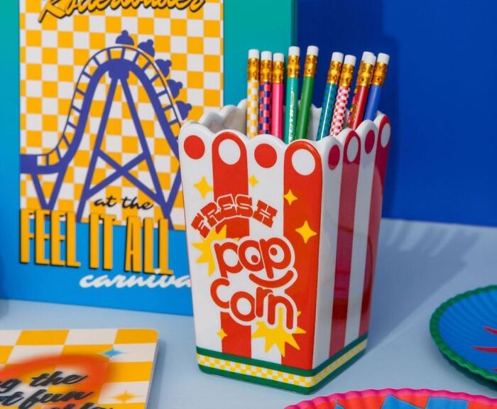 Popcorn-themed pencil holder, an impulse buy, with colorful pencils in front of carnival-themed decor.