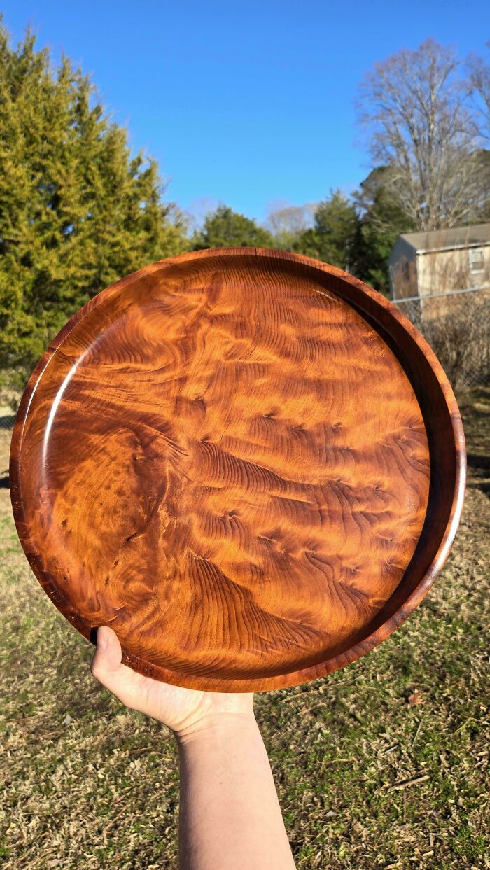 Hand holding a beautifully carved wooden tray showcasing intricate woodworker craftsmanship outdoors on a sunny day.