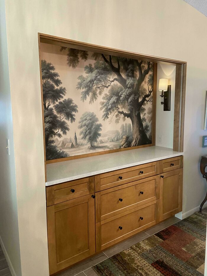Built-in wooden cabinet with white countertop and scenic tree mural, showcasing beautifully decorated homes interior design.