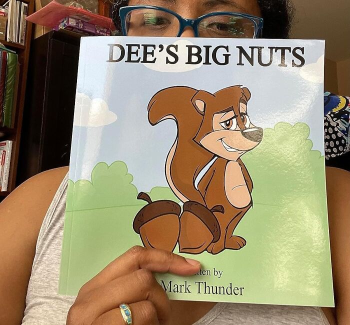A person holding a book titled "Dee's Big Nuts" with a cartoon squirrel on the cover.
