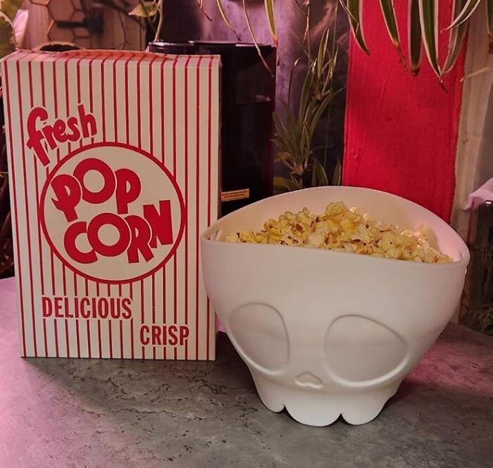 Skull-shaped bowl filled with popcorn next to a striped popcorn box on a counter.