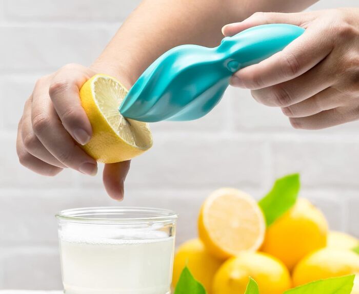 Weird kitchen item, a turquoise lemon squeezer, used to extract juice into a clear glass.