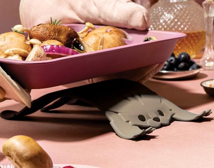 Quirky kitchen item tray lifter shaped as a playful animal, elevating a purple tray with food, on a dining table.