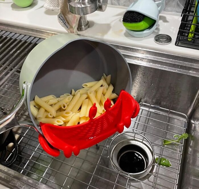 Pasta being drained with a red strainer clip, showcasing a weird kitchen item in use over a sink.