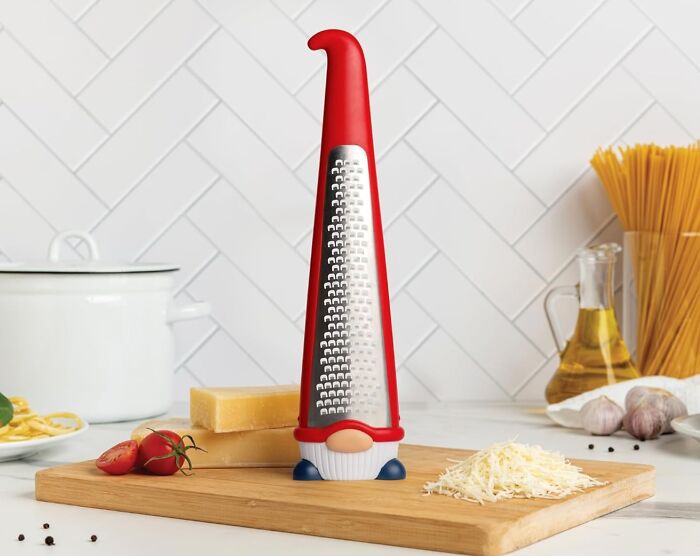 Weird kitchen item shaped like a gnome, used as a cheese grater, on a cutting board with ingredients around.