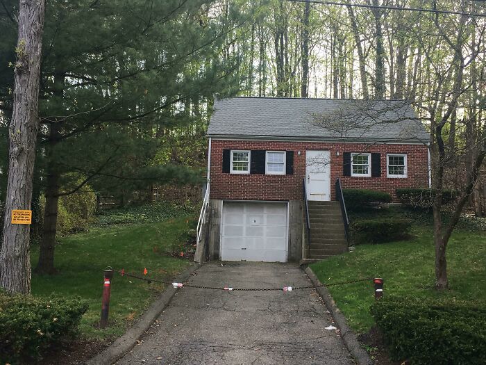 A small brick house with a garage, surrounded by trees. Cities-Genius-Solutions.