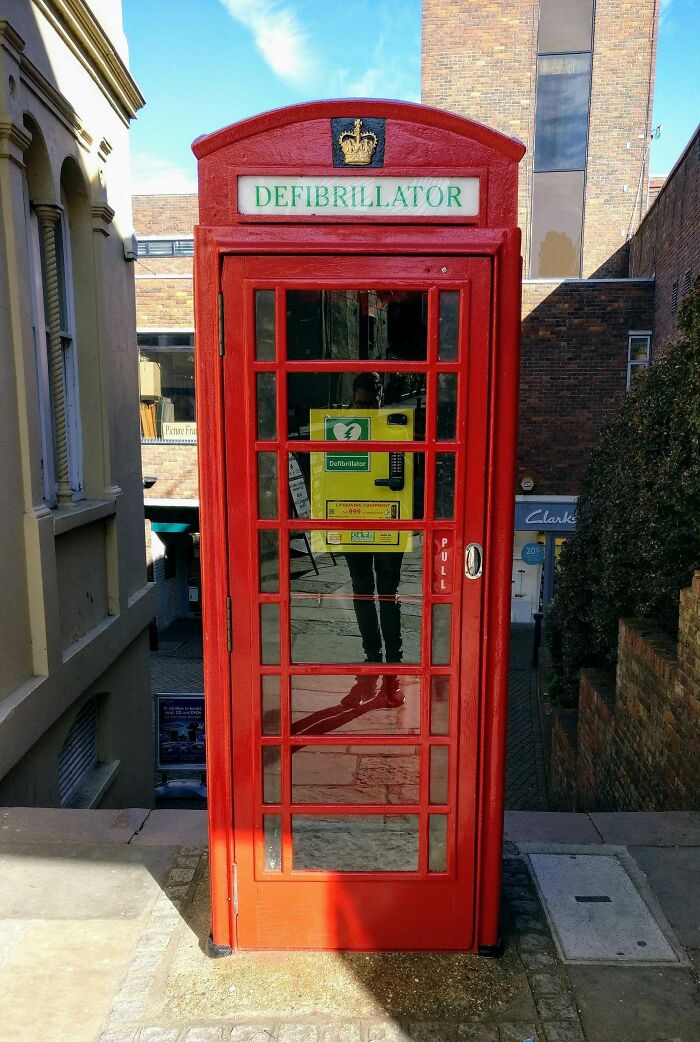 Red phone booth repurposed as a defibrillator station in an urban setting, showcasing Cities-Genius-Solutions.