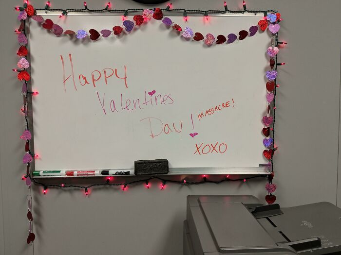 Valentine's board with heart garland, lights, and festive message, alongside a printer, embodying weird yet cute décor.