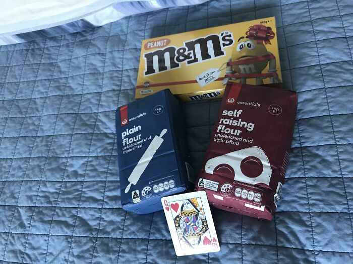 Weird yet cute Valentine's gifts: M&Ms, flour bags, and a queen of hearts card on a bedspread.