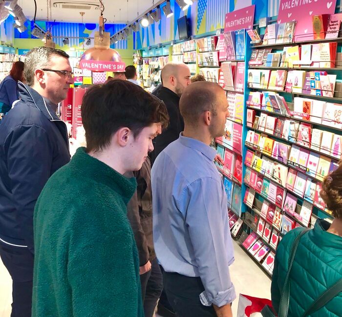 People browsing Valentine's Day cards in a store, surrounded by a variety of colorful and quirky gift options.
