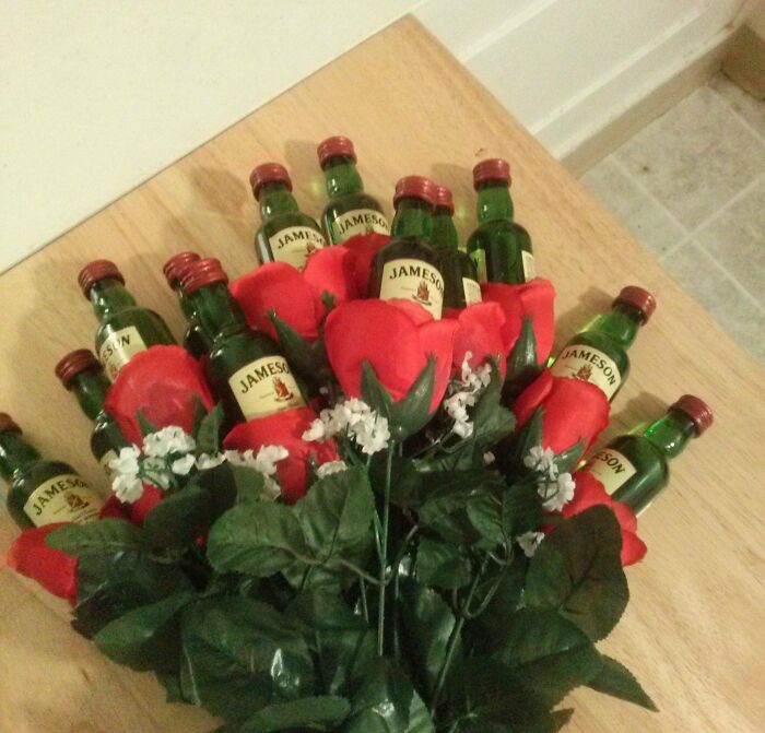 Bouquet of roses with mini whiskey bottles, a cute and weird Valentine's gift arrangement on a wooden table.