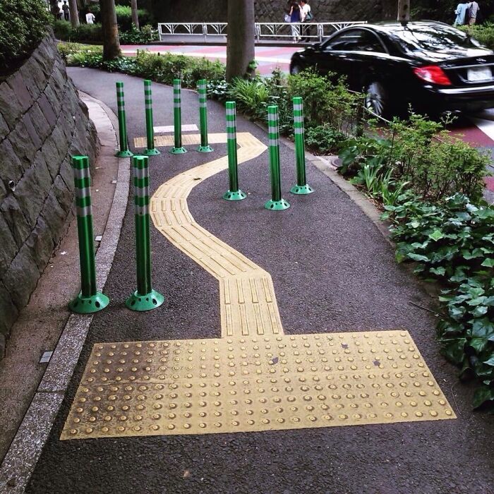 Tactile path obstructed by green poles on a sidewalk, highlighting creative urban solutions.