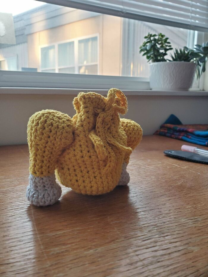 Crochet masterpiece of a yellow turkey placed on a wooden table near a window with plants in the background.