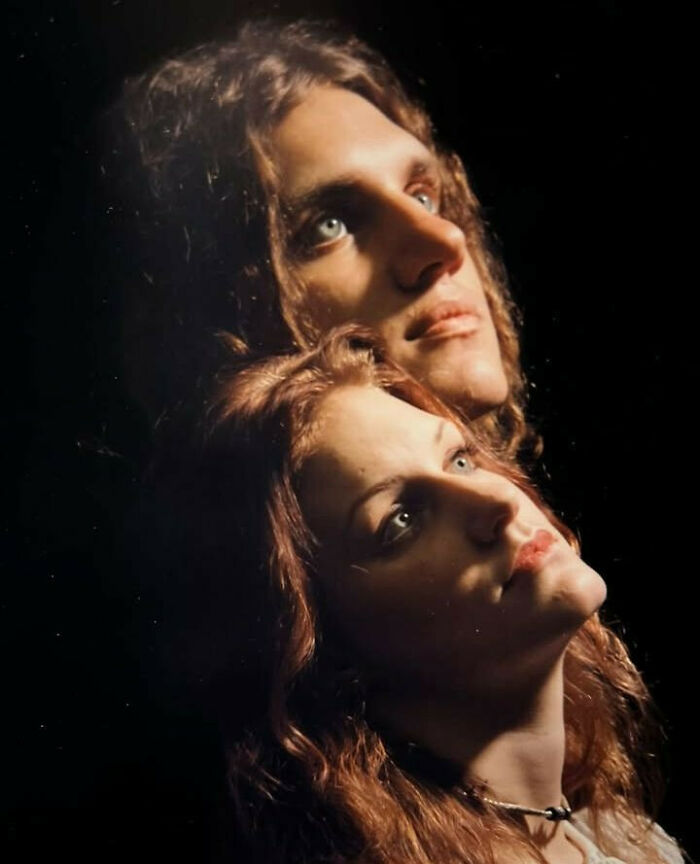 Two people with curly hair pose in an awkward but sweet family photo against a dark background.
