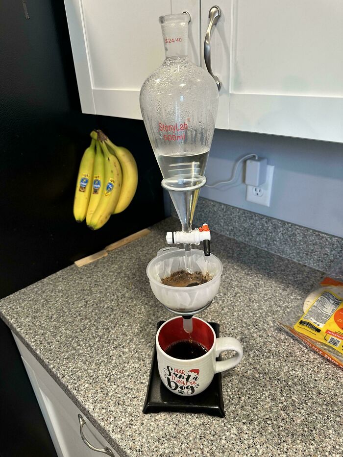 Homemade coffee maker setup using a chemistry funnel and flask on a kitchen counter with bananas in the background