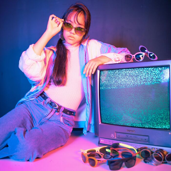 Young woman in retro attire with sunglasses and vintage TV, showcasing 2025-Trends.