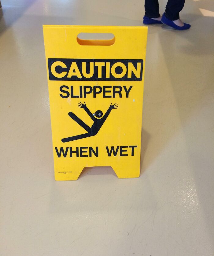 Yellow caution sign in public area featuring a funny image of a person slipping, highlighting the message "Caution Slippery When Wet."