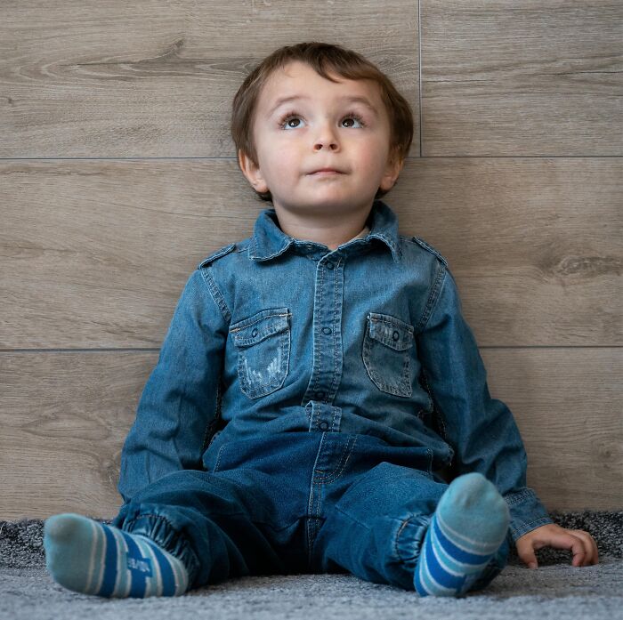 Young child in denim outfit sitting indoors, looking upwards, representing 2025-Trends in kids' fashion.