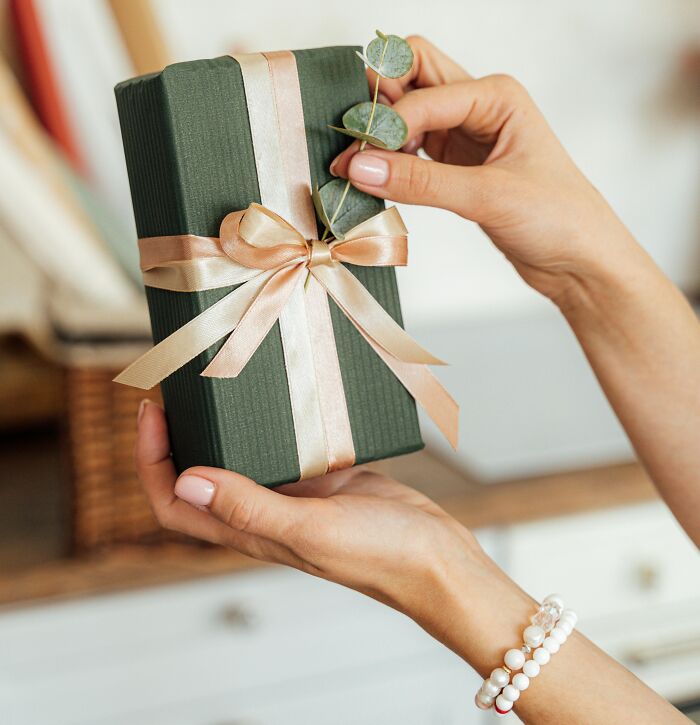 Hands holding a green gift box with ribbon and leaves, showcasing 2025-trends in gift wrapping styles.