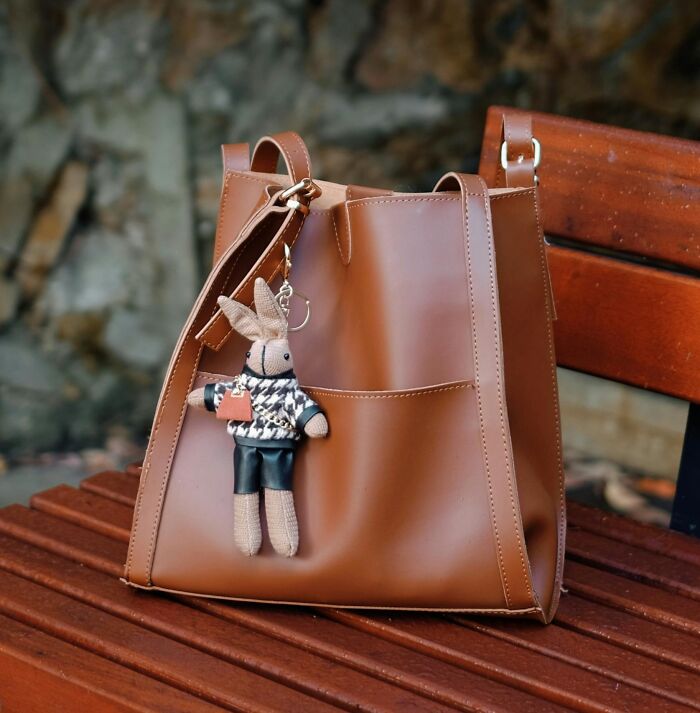 Brown leather bag with plush keychain, highlighting 2025 trends in fashion accessories, placed on a wooden bench.
