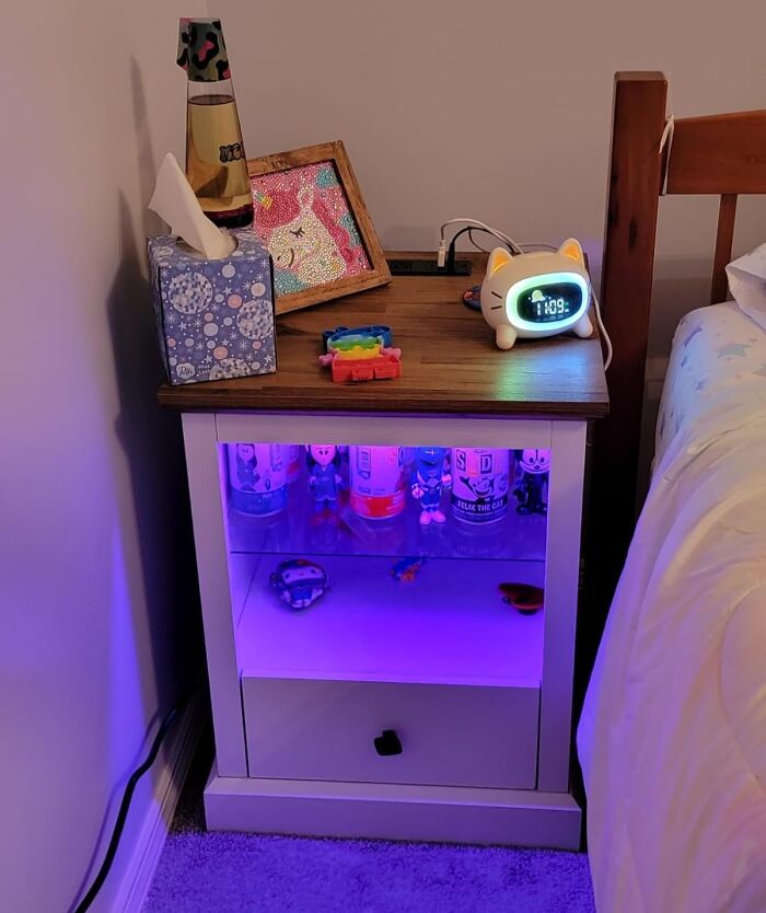 Modern nightstand with LED lighting, featuring toy figurines and a cute cat-shaped clock, reflecting 2025 interior trends.