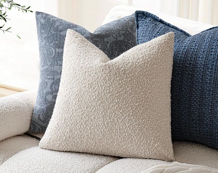 Soft textured pillows in neutral and blue hues on a sofa, highlighting 2025 interior trends in home decor.
