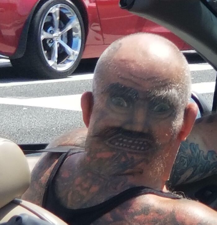 "Man in Florida with face tattoo on the back of his head, creating a wild optical illusion while seated in a convertible car."