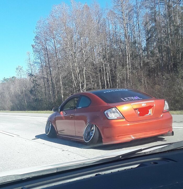 Lowered orange car on Florida highway, showcasing wild vehicle modifications with extreme wheel camber.