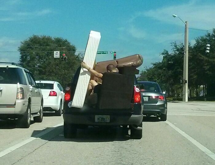 Overpacked truck on a Florida road, filled with furniture and a person holding onto a mattress.