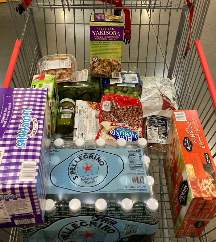 Shopping cart filled with groceries including bottled water, snacks, and frozen meals, illustrating grocery-shopping-hacks.