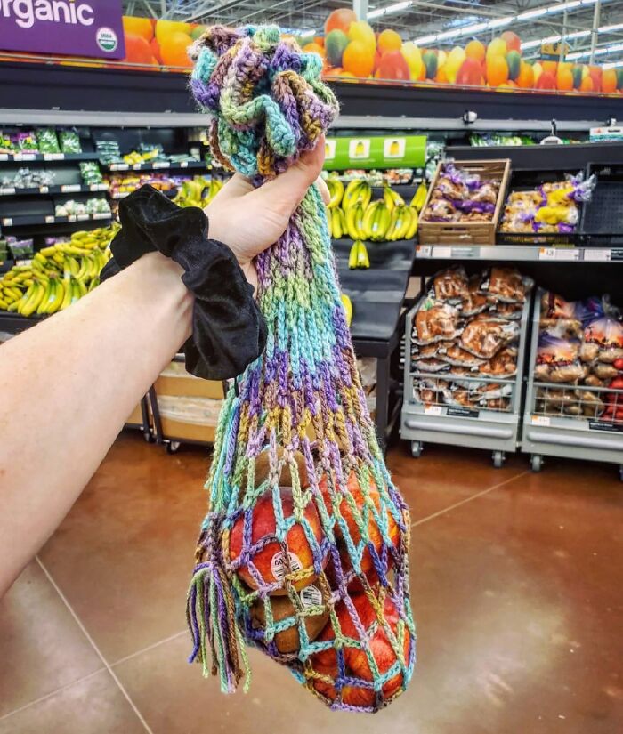 Hand holding a colorful reusable net bag with apples in a grocery store, showcasing grocery-shopping-hacks.