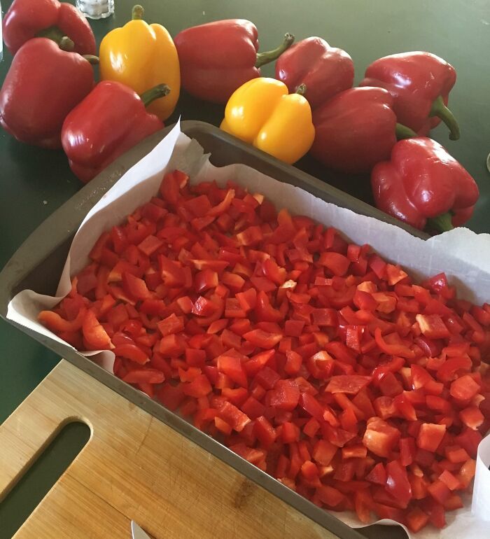 Chopped red bell peppers in a baking tray, with fresh peppers on a kitchen counter. Grocery-shopping-hacks for meal prep.