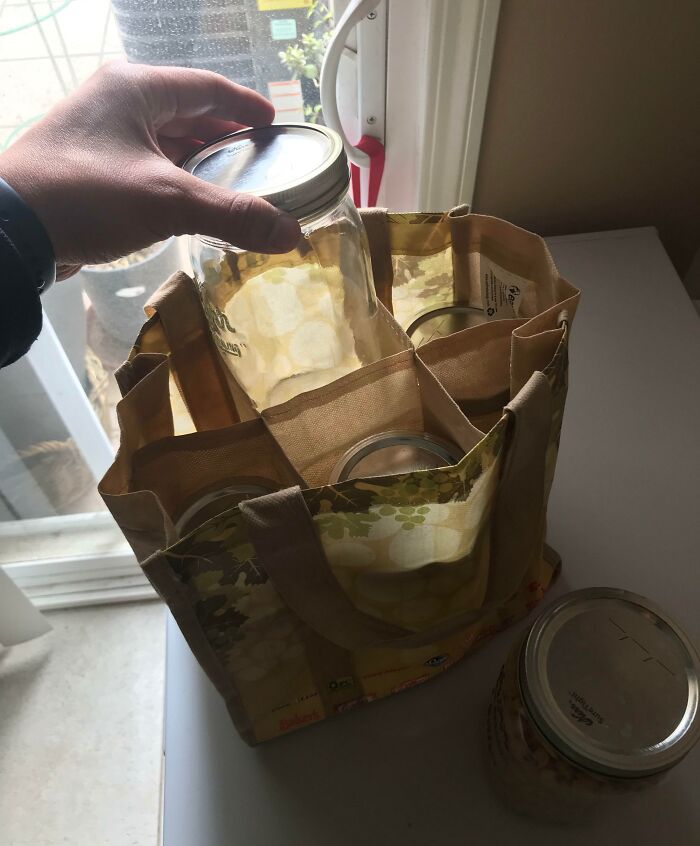 Hand holding a jar over a cloth grocery bag with jars inside, illustrating grocery-shopping-hacks for zero waste.