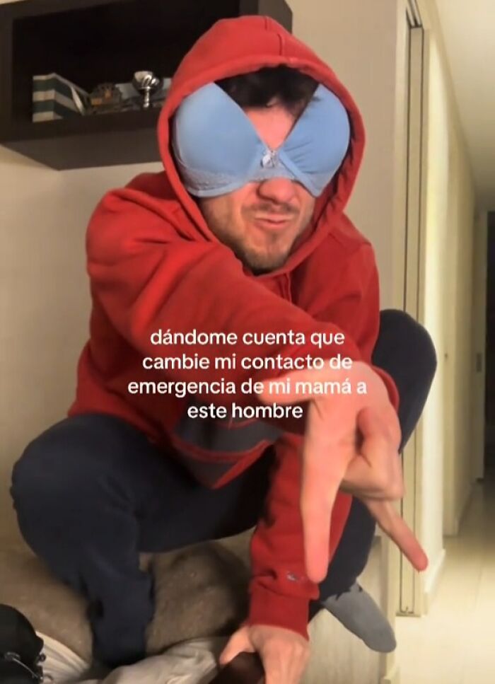 Man wearing a red hoodie and blue bra over eyes, posing humorously.