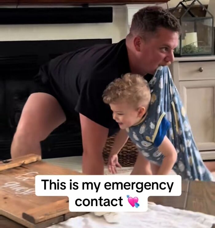 Man playing with child wrapped in a blanket, crawling on the floor in a humorous home setting.