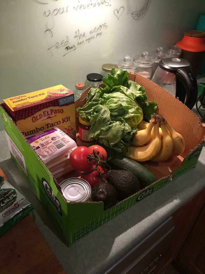 Box of assorted groceries including lettuce, bananas, and taco kit, illustrating grocery-shopping-hacks on a kitchen counter.