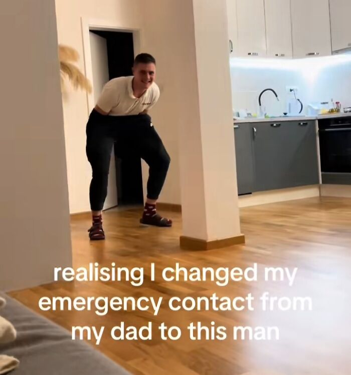 Man jokingly poses in a kitchen, wearing mismatched socks, representing a humorous emergency contact crisis.