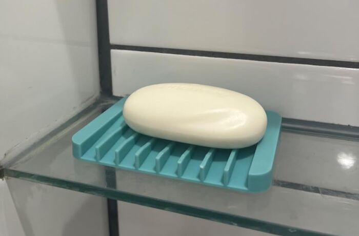 White bar of soap on a blue soap holder inside a glass shower shelf, affordable items under 5 dollars concept.