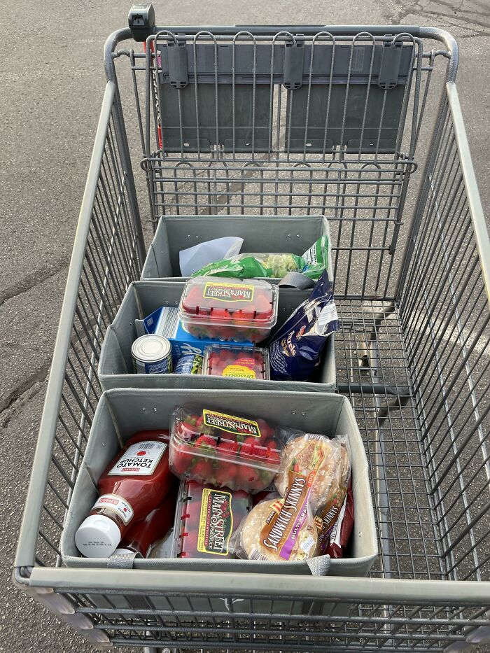 Shopping cart organized with bins, containing groceries like strawberries and bread, showcasing grocery-shopping-hacks.