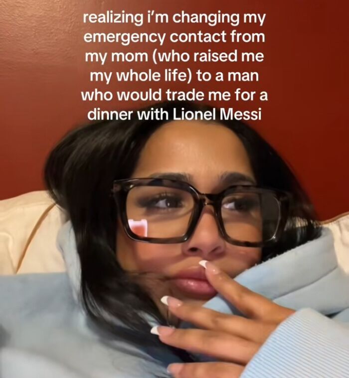 Woman in a hoodie and large glasses, pondering emergency contacts and humorous relationship decisions.