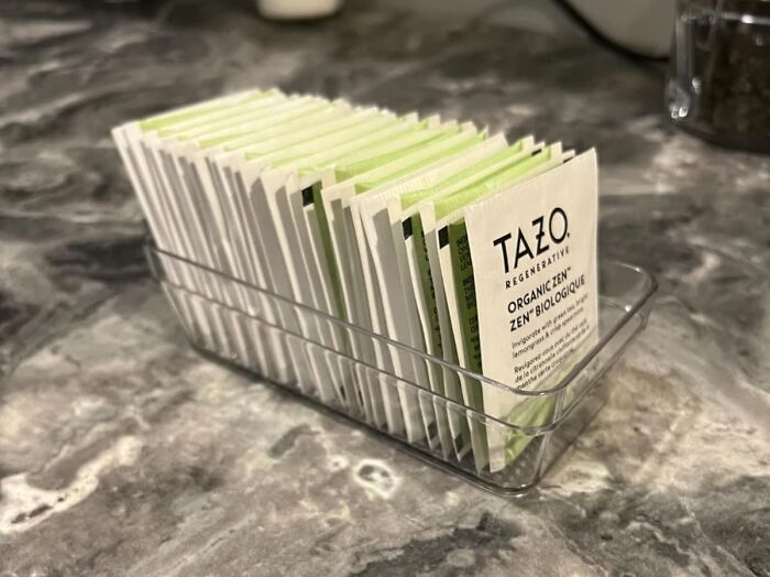 Clear container holding neatly arranged Tazo tea bags on a marble countertop, affordable items under $5.