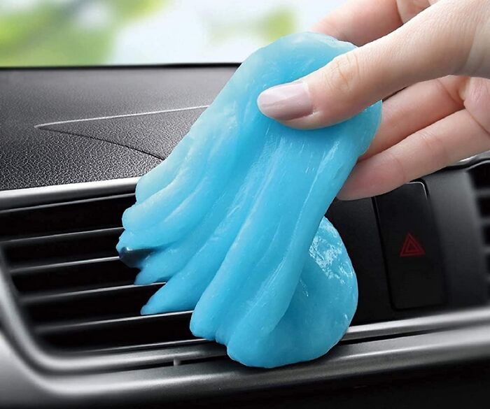 Hand holding blue cleaning gel removing dust from car air vent, a surprising item under 5 dollars for saving coins.