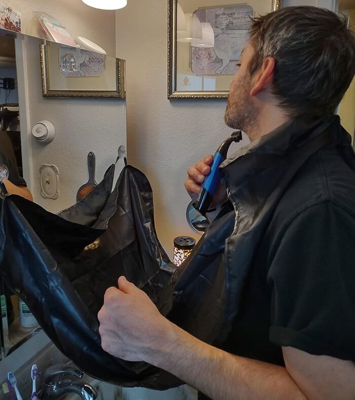Man using a beard trimming apron in a bathroom mirror, demonstrating an affordable grooming tool under $5.