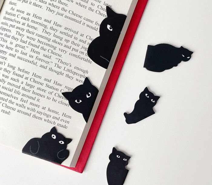 Black cat-shaped bookmarks marking pages in an open book, affordable savings idea under 5 dollars for book lovers.