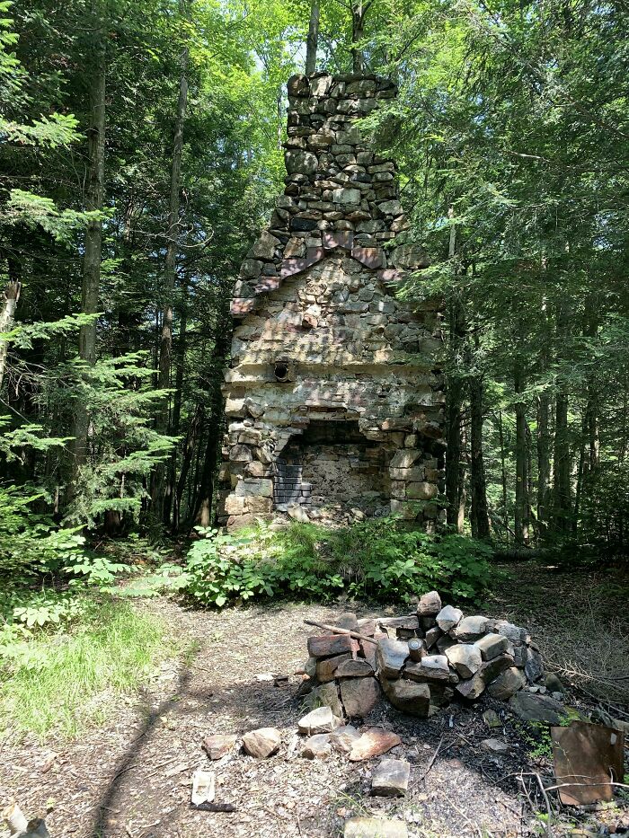 Old stone chimney in the forest, covered by nature, exemplifying nature reclaiming civilization.