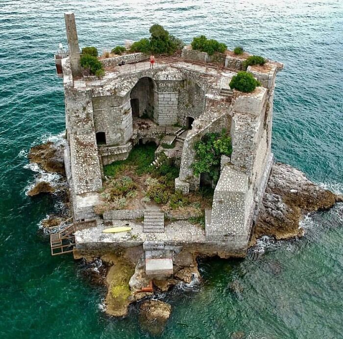 Abandoned stone fortress surrounded by sea, with greenery growing as nature reclaims civilization.