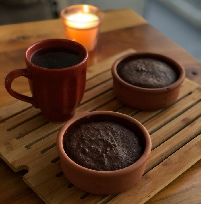 Two small chocolate cakes and a cup of coffee on a wooden board, creating eye-opening moments with a lit candle in the background.